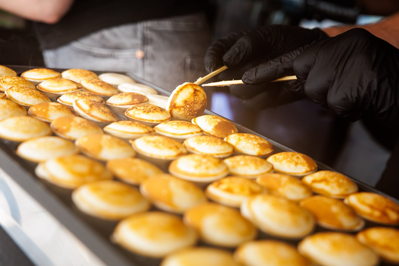 Verse poffertjes worden gekeerd op de bakplaat